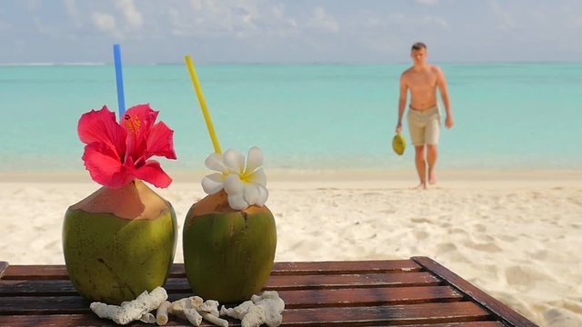 Tropical fresh coconut cocktail on white beach. Two coconut drinks on luxury tropical resort in Maldives island. Fresh green coconut cocktails on sandy Maldives beach with turquoise sea background.