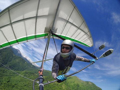 Hang glider pilot soaring the thermal updrafts above green mountain hills