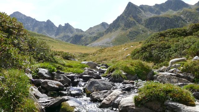 Landscape of a mountain creek, on the Pyrenees of Andorra. Little brook with the mountains in the background and with the brightness of the sky in the water.
