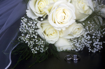Wedding background, good for greeting cards or invitations. Close up horizontal composition with white roses bride bouquet, veil and wedding rings on a foreground. Starting family concept.