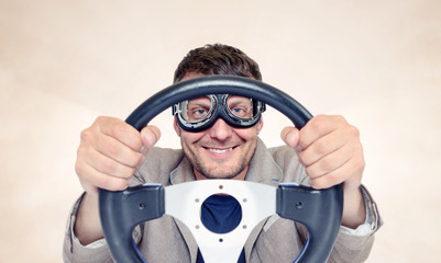 Bearded happy man in stylish goggles with steering wheel on background, car driver concept