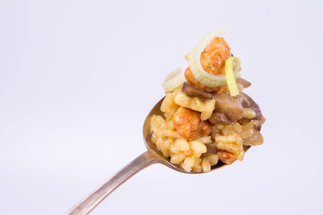 Risotto with mushrooms and chicken decorated with leek on a spoon on a white background