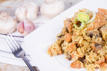 Risotto with mushrooms and chicken decorated with leek on a wooden background 