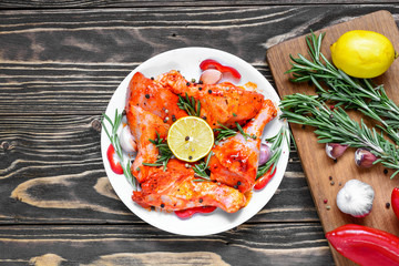 raw marinated chicken legs with red spicy sauce and herbs in a plate on wooden background with cutting board