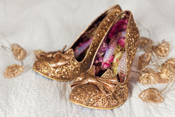 A brides beautiful, golden, glittery, sexy pair of individual stylish wedding shoes, on a white creamy material surface.