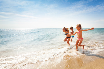 Happy friends running along edge of sea in summer - Powered by Adobe