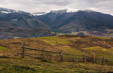 wooden fence on hills of mountainous countryside. agricultural fields in late autumn gloomy weather. mountain ridge with snowy tops in the distance