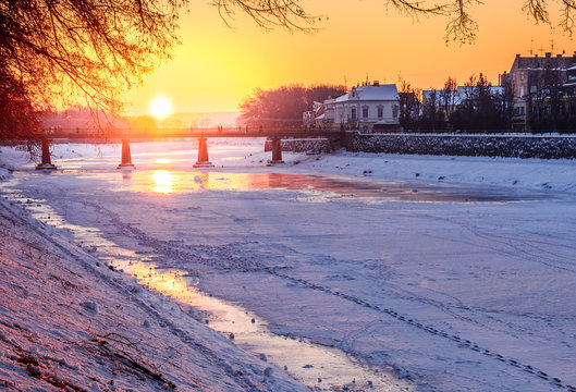 winter sunrise on the bank of ice covered river Uz. Sun over the bridge of old European town Uzhgorod