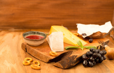Tasting cheese dish with herbs and fruits on old wooden table. Food for wine party, cheese delicatessen. Close-up.