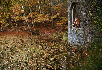 Pre- Raphaelite looking woman with long red hair posing wistfully in the open window of a Gothic tower