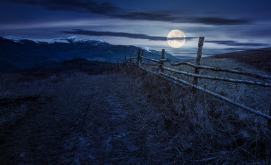 wooden fence in mountainous countryside at night in full moon light. mountain ridge with snowy tops...