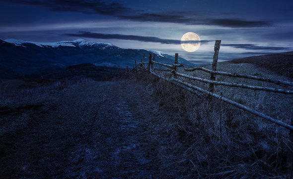 wooden fence in mountainous countryside at night in full moon light. mountain ridge with snowy tops in the distance