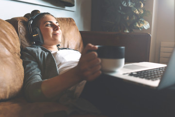 Attractive young happy girl listening to music in headphones with pleasure at coworking office,...