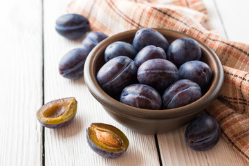 Fresh plums in ceramic bowl on white wooden background.