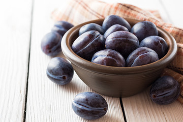 Fresh plums in ceramic bowl on white wooden background.