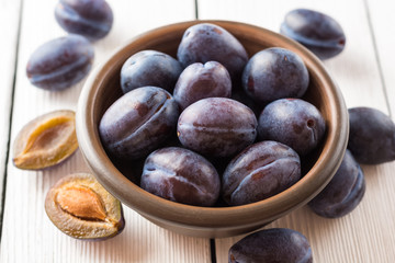 Fresh plums in ceramic bowl on white wooden background.