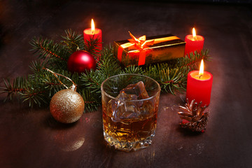 christmas decoration with glass of cognac or whiskey, red candles, gift box and christmas tree. Selective focus.