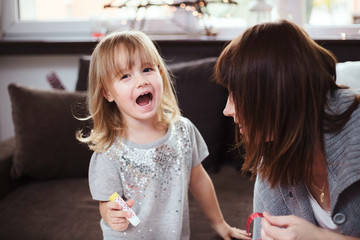 Young girl laughing while making paper decorations with her mother.