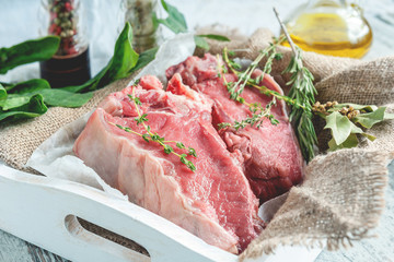Cuts of beef for grilling on a wooden cutting Board with spinach, rosemary and Provencal herbs for the marinade in a rustic style.