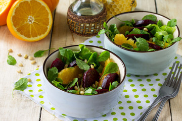 Homemade snacks on the kitchen wooden table. Salad with beets, orange, arugula and pine nuts.