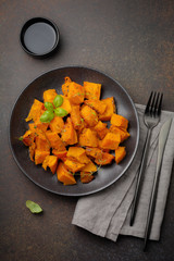 Fried pumpkin slices with herbs and pepper, olive oil in a black ceramic plate on  dark concrete or stone background. Selective focus. Top view.