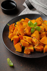 Fried pumpkin slices with herbs and pepper, olive oil in a black ceramic plate on  dark concrete or stone background. Selective focus.