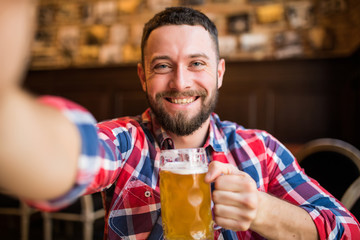 people and technology concept - man with smartphone drinking beer and taking selfie at bar or pub