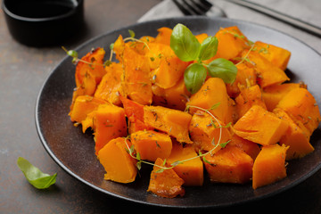 Fried pumpkin slices with herbs and pepper, olive oil in a black ceramic plate on  dark concrete or stone background. Selective focus.