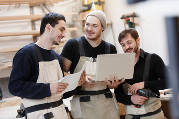 Master of small business with laptop and his team as sign of innovation in carpenter workshop....