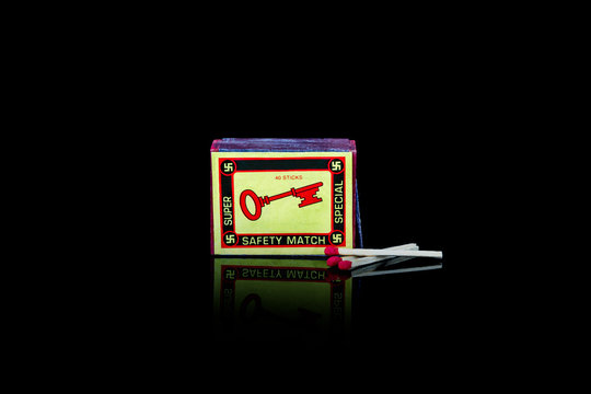 A vintage match box with swastikas and a key  on the front. Isolated studio shot on black background.