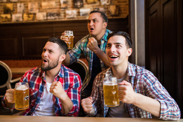 Men fans watching football on TV and drink beer. Three other men drinking beer and having fun together in the bar