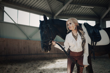 Beautiful elegant young blonde girl standing near her horse dressing uniform competition