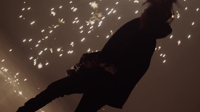 Guitar player with dreadlocks rocks out while awesome sparks rain down