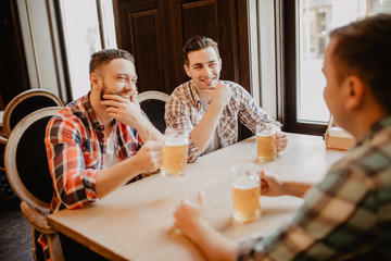 Cheerful friends having fun and drinking draft beer in pub.