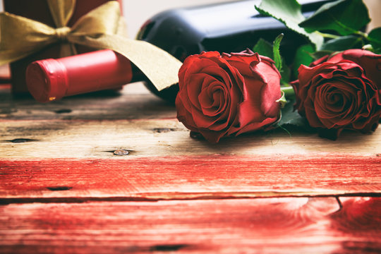 Valentines Day. Red Wine Bottle, Roses And A Gift On Wooden Background