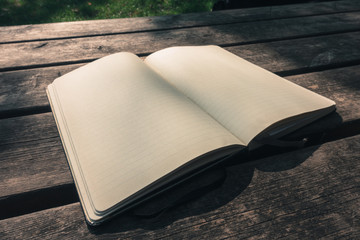 Blank empty moleskine notepad in three quarters view from top on wooden table in a park