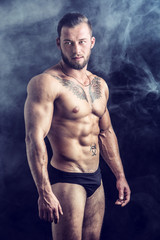 Muscular young man standing and looking to a side, shirtless, wearing briefs, showing chiselled...