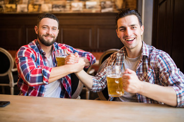 Happy young bearded man laughing high fiving his friend while having beer at the pub together