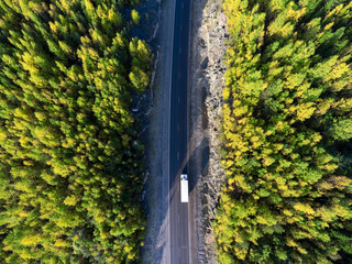 Top view at white freight truck driving between rock tunnel in golden autumn forest of Karelia,...