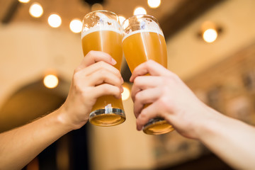 Close up og Mens hands cheers with beer in glasses in pub.