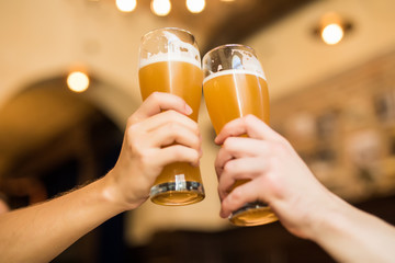 Close up og Mens hands cheers with beer in glasses in pub.
