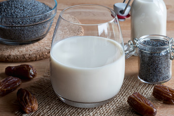 A glass of poppy seed milk with poppy seeds in the background