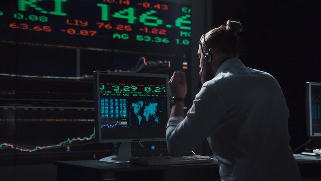 Young male entrepreneur working in office of exchange and driving lively trade while speaking with headset.