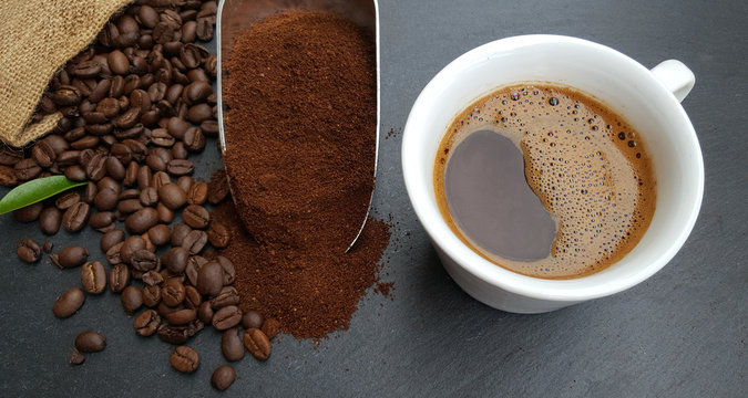 Coffee cup, beans and ground powder on dark  background