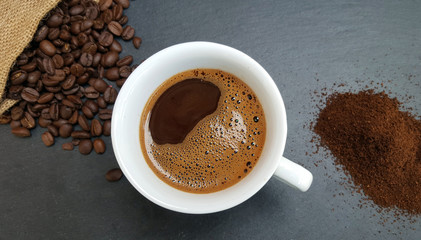 Coffee cup, beans and ground powder on dark  background