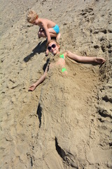 Mädchen ist im Sand eingegraben und kleiner Junge sitzt daneben