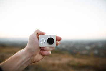 Man holds an action camera on the sunset background