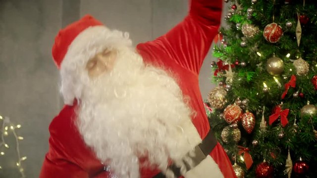 Bearded Santa Claus doing gymnastics on background New Year tree