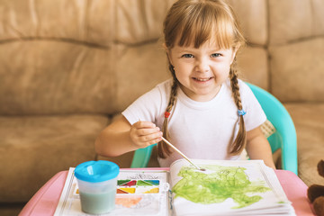 Little girl coloring drawings sitting at the table, child development