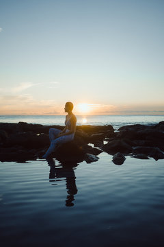 woman sitting by oceanside while sunset
